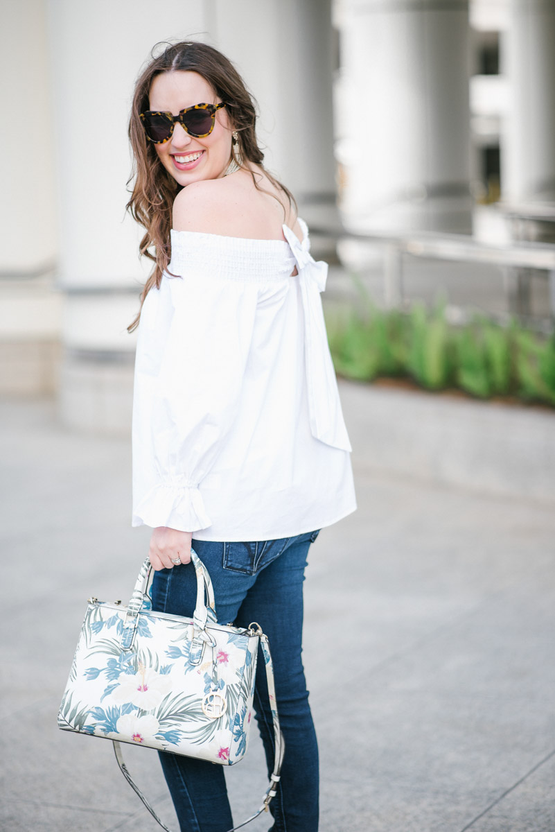 Houston fashion blogger styles a white off the shoulder bow back top with a Henri Bendel floral handbag and Steve Madden wedges for spring outfit inspiration.
