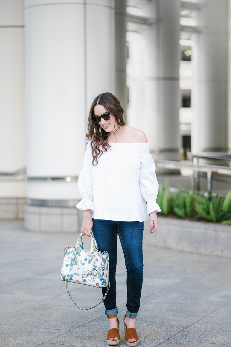 Houston fashion blogger styles a white off the shoulder bow back top with a Henri Bendel floral handbag and Steve Madden wedges for spring outfit inspiration.