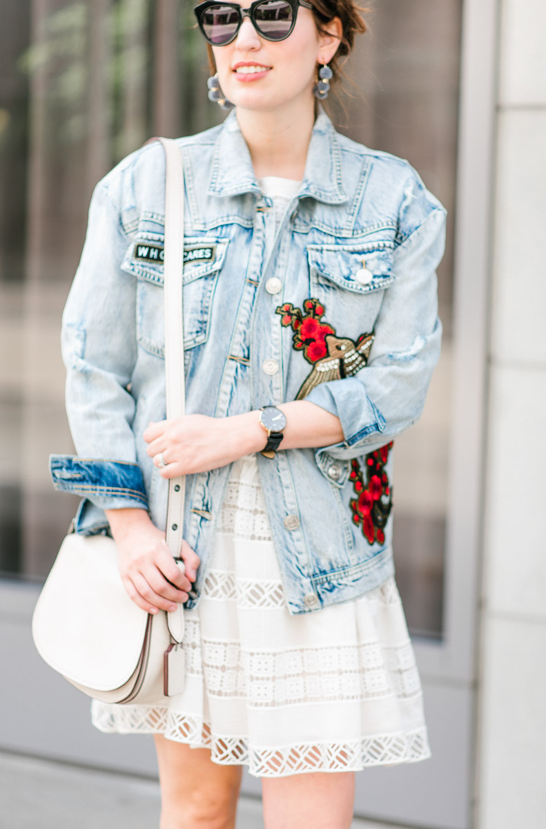 Embroidered denim jacket with a white coach saddlebag.