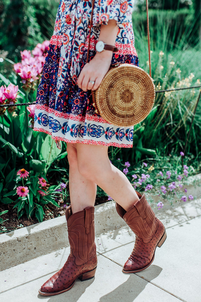 How to wear cowboy boots in the Summer featured by top US fashion blog, Lone Star Looking Glass: image of a woman wearing a floral Eliza J dress, Stree Level Crossbody bag, Daniel Wellington watch, Red Dress earrings and Tecovas cowboy boots for women