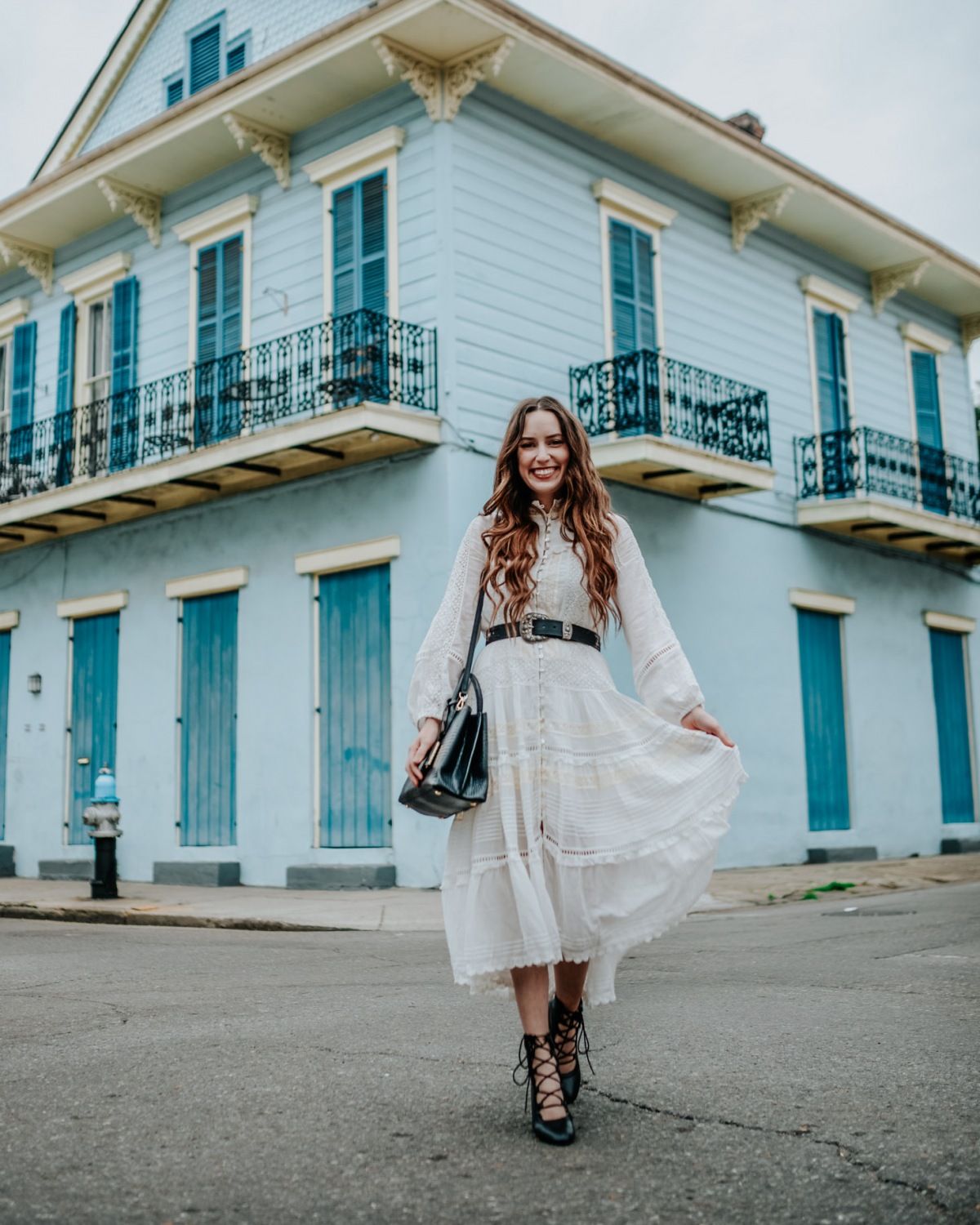 Houston blogger, white spell embroidered dress, new orleans french quarter blue building | The perfect Boho White Dress for Spring styled by top US fashion blog, Lone Star Looking Glass: image of a woman wearing a Hanging Rock Gown boho white dress available at Shopbop, Free People studded belt, trench booties and an Anthropologie mini tote