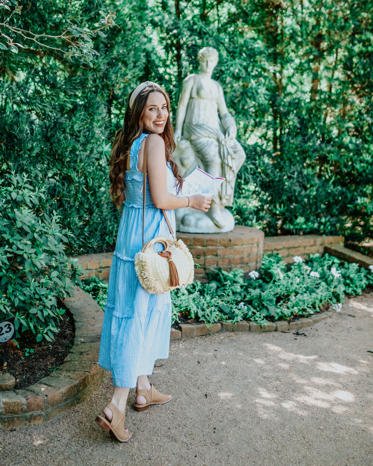 Visiting Bayou Bend Gardens in the Spring featured by top US travel and fashion blog, Lone Star Looking Glass: image of a woman walking through Bayou Bend Gardens wearing a Gal Meet Glam maxi dress, Anthropologie rafia headband and Sofft sandals