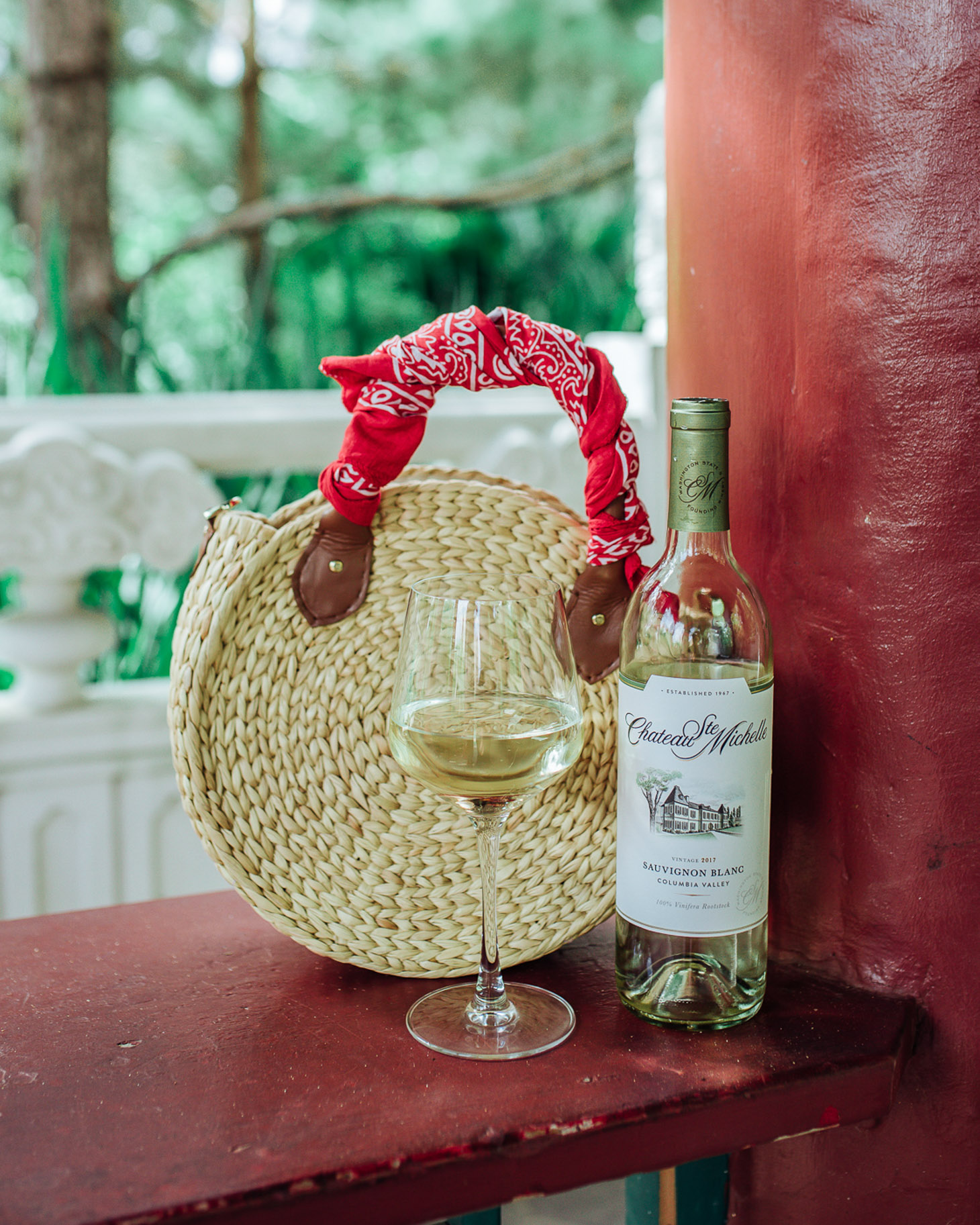 A Thoughtful Hostess Gift for Every Occassion by popular Texas lifestyle blog, Lone Star Looking Glass: image of a bottle and glass full of Chateau Ste. Michelle wine next to a woven circular purse. 