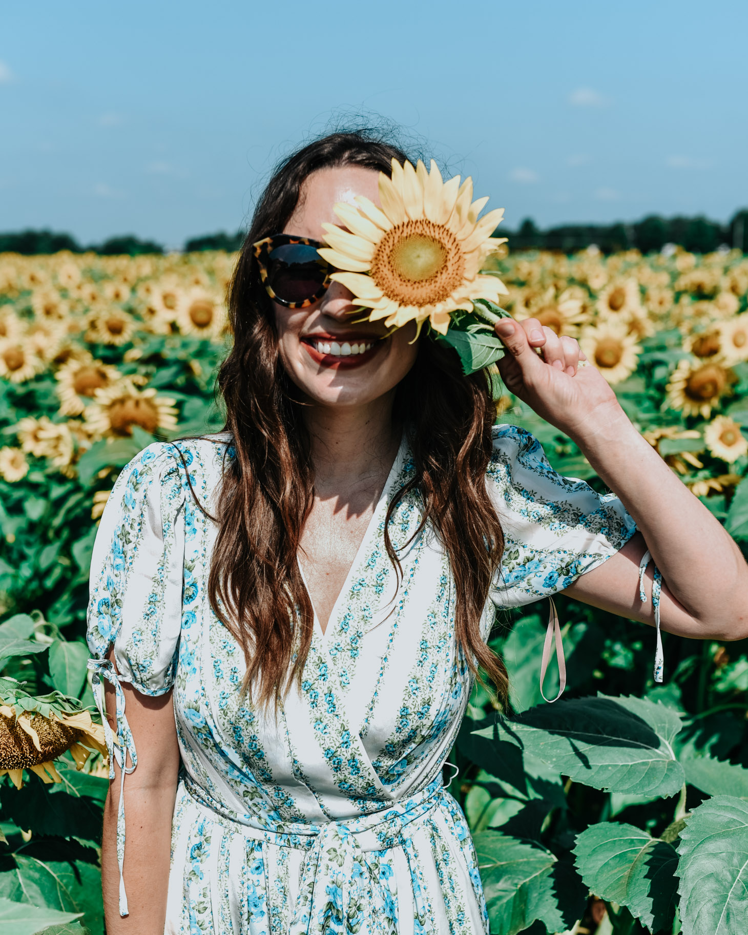 5 Dress Designers to Take Note Of this Summer by popular Memphis fashion blog, Lone Star Looking Glass: image of a woman standing in a sunflower field, holding a sunflower up to her face, and wearing a Gal Meets Glam Dress.