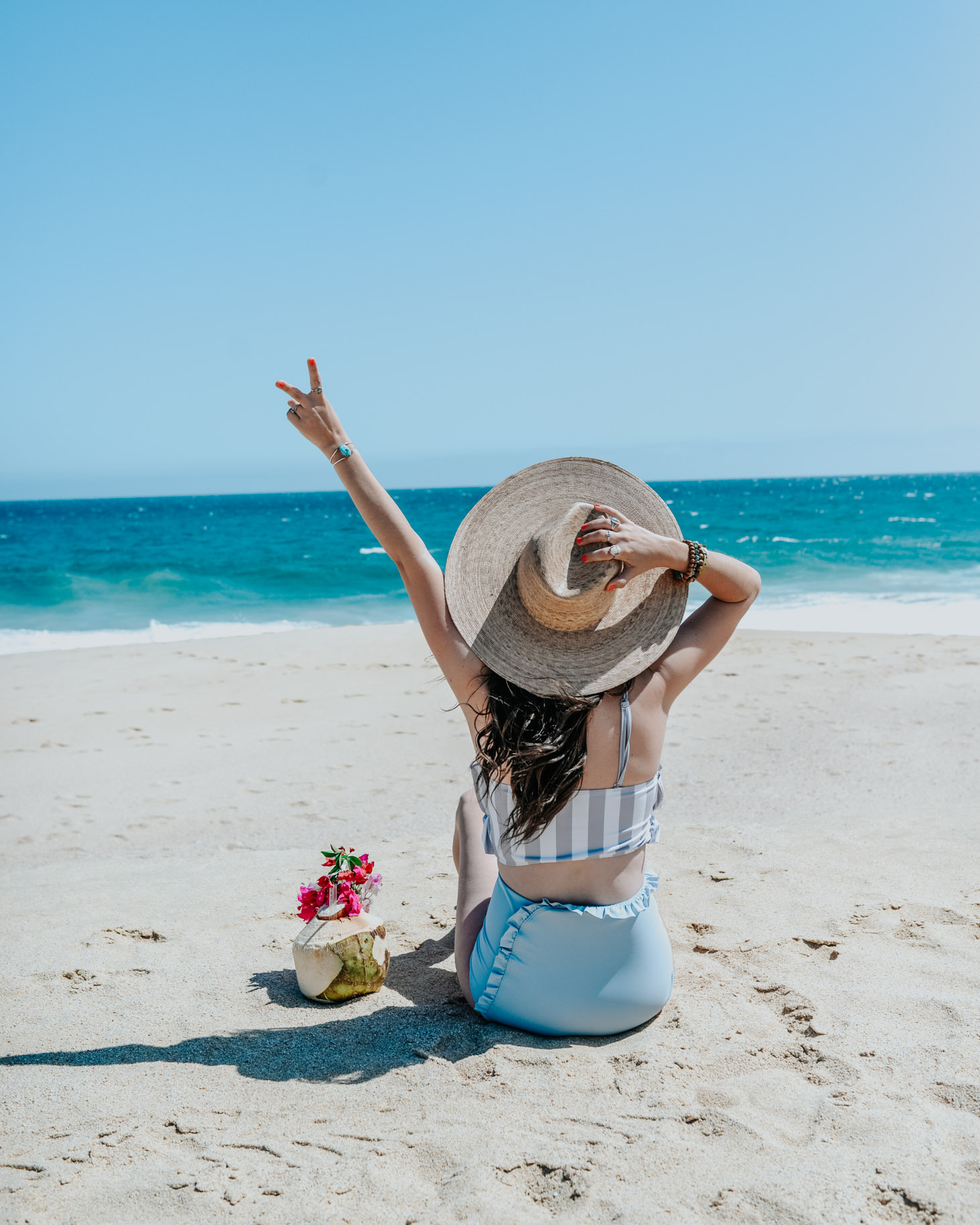 Pueblo Bonito Pacifica: 8 Reasons to Vacation in Cabo by popular Tennessee travel blog, Lone Star Looking Glass: image of a woman sitting on the beach with a coconut drink. 