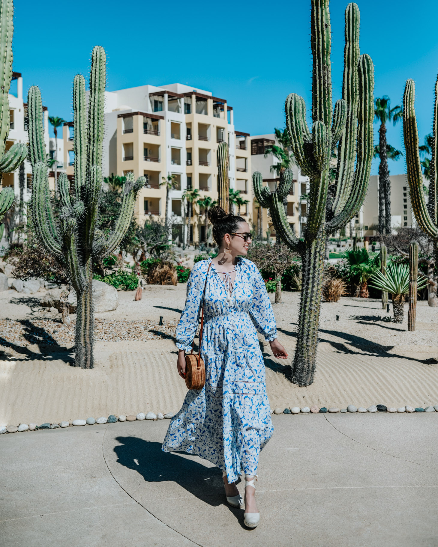 Pueblo Bonito Pacifica: 8 Reasons to Vacation in Cabo by popular Tennessee travel blog, Lone Star Looking Glass: image of a woman walking by some cacti and wearing a maxi dress and espadrilles and carrying a straw bag. 