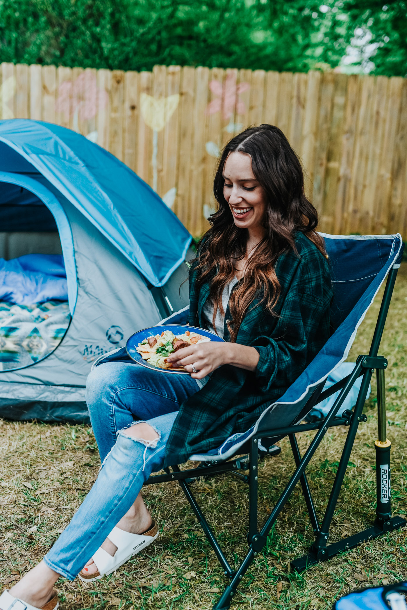Backyard Camping by popular Memphis lifestyle blog, Lone Star Looking Glass: image of a woman wearing a Academy BCG Women's Slub Solid T-shirt and Academy Carhartt Women's Rugged Flex Hamilton Flannel Work Shirt and eating some nachos while sitting in a Academy GCI Outdoor Pod Rocker. 