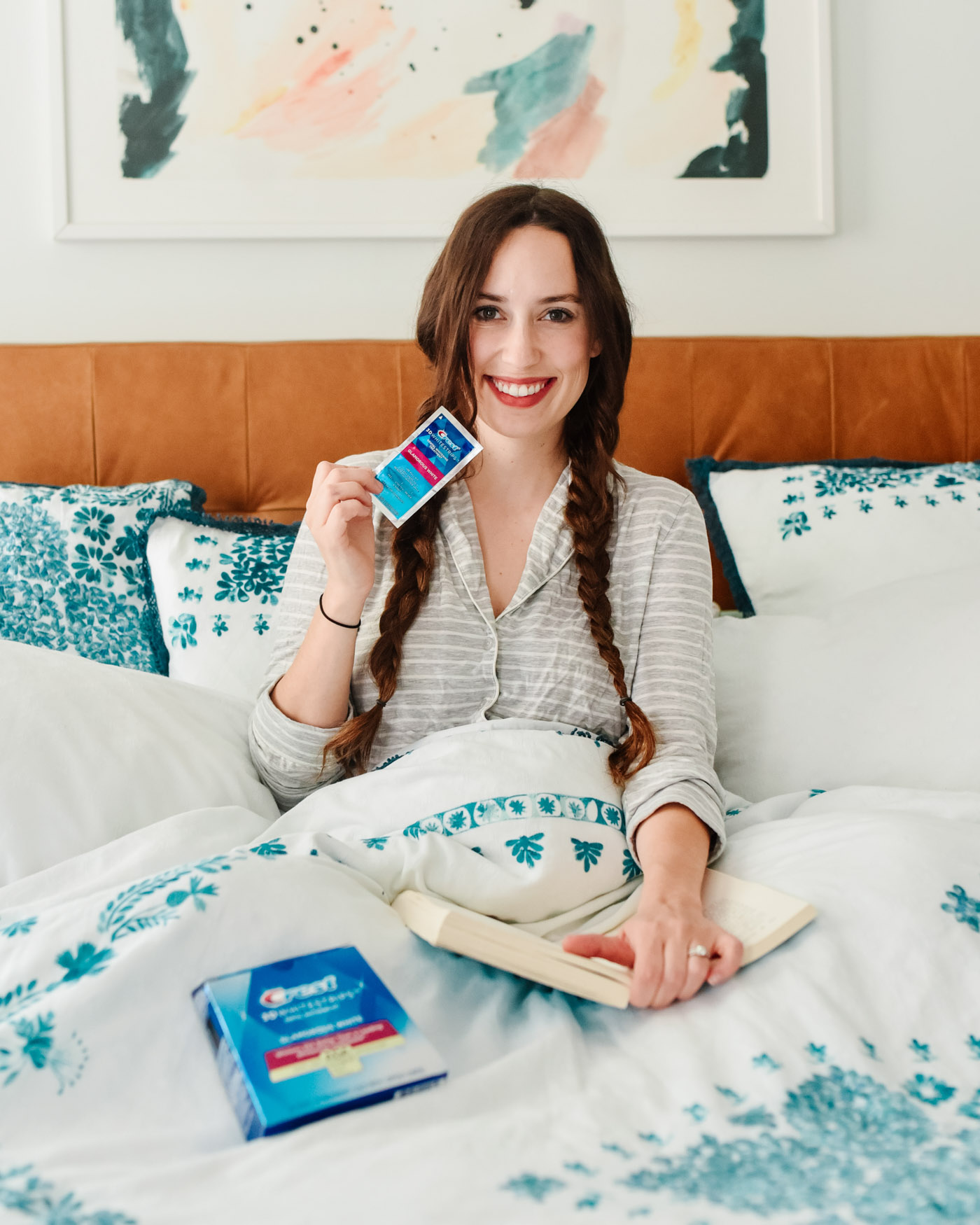 Crest 3D Whitestrips by popular Memphis lifestyle blog, Lone Star Looking Glass: image of a woman sitting in bed with a book in her lap and holding some Crest 3D Whitestrips. 
