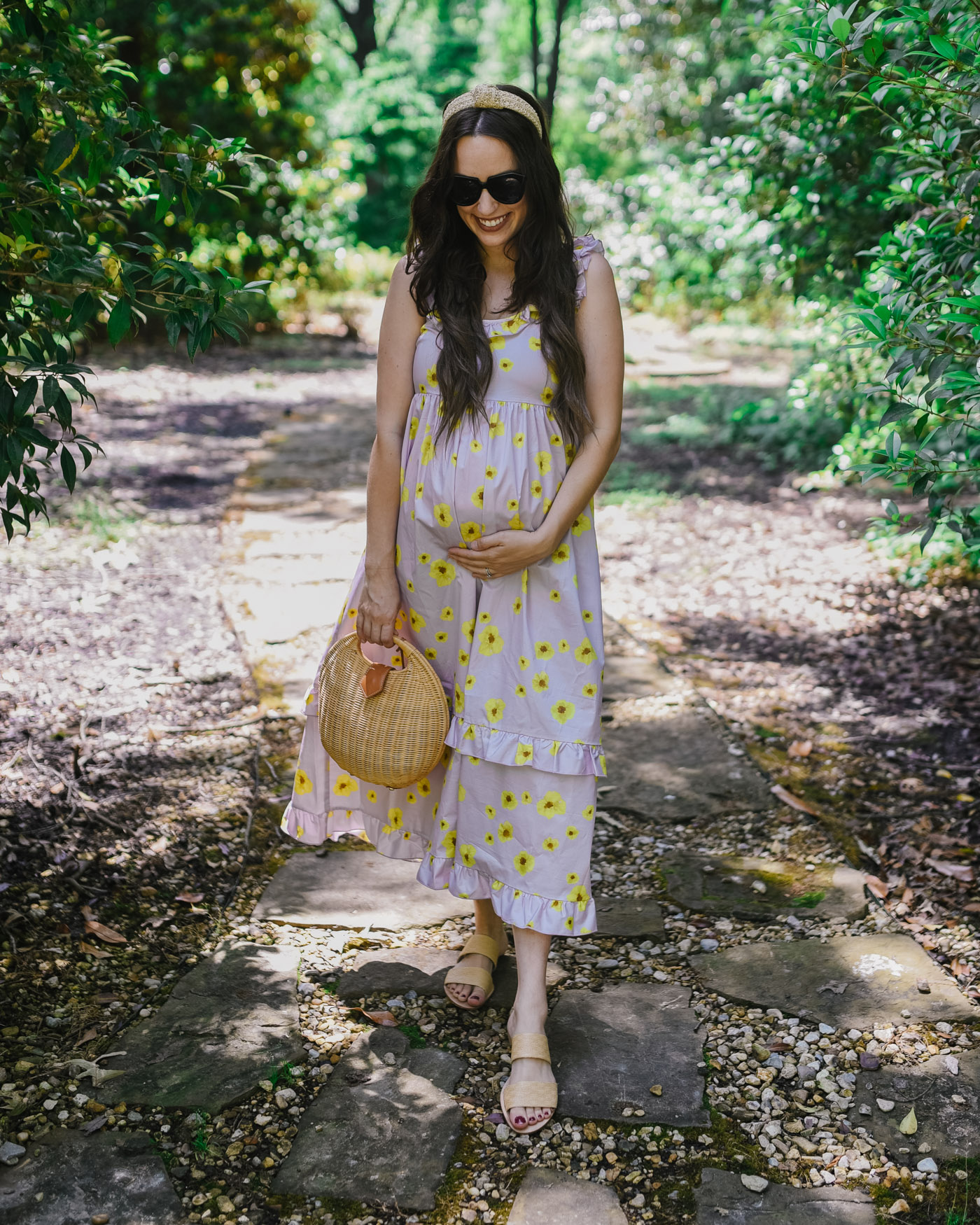 Pregnancy Tips by popular Memphis motherhood blog, Lone Star Looking Glass: image of a woman standing outside on a stone path and wearing a Hatch The Rafaela Dress, Knotted raffia headband, black sunglasses, and Raye Judah Slide.