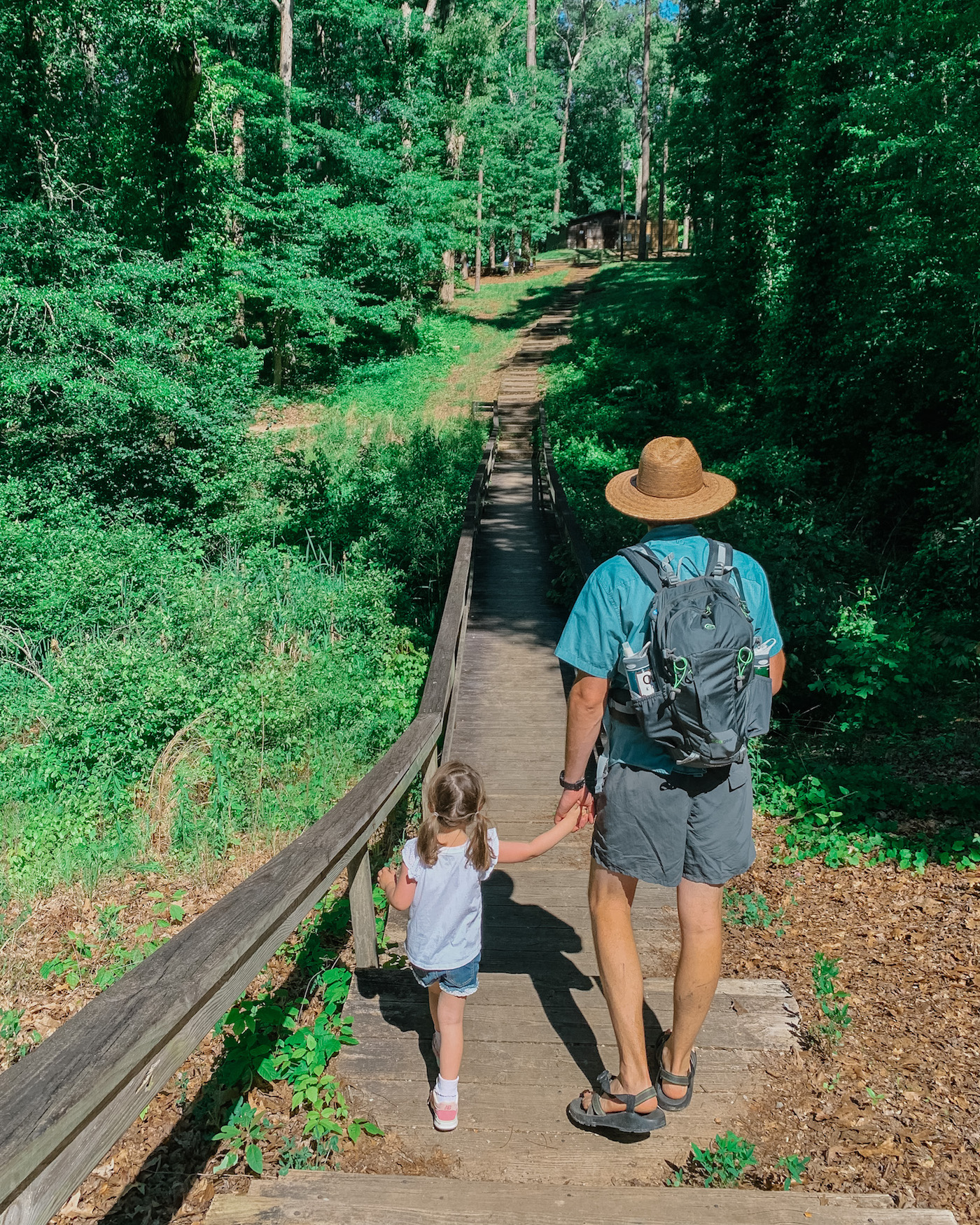 Father's Day Gift Ideas by popular Memphis lifestyle blog, Lone Star Looking Glass: image of a dad and his young daughter holding hands while walking on a boardwalk in a forest. 