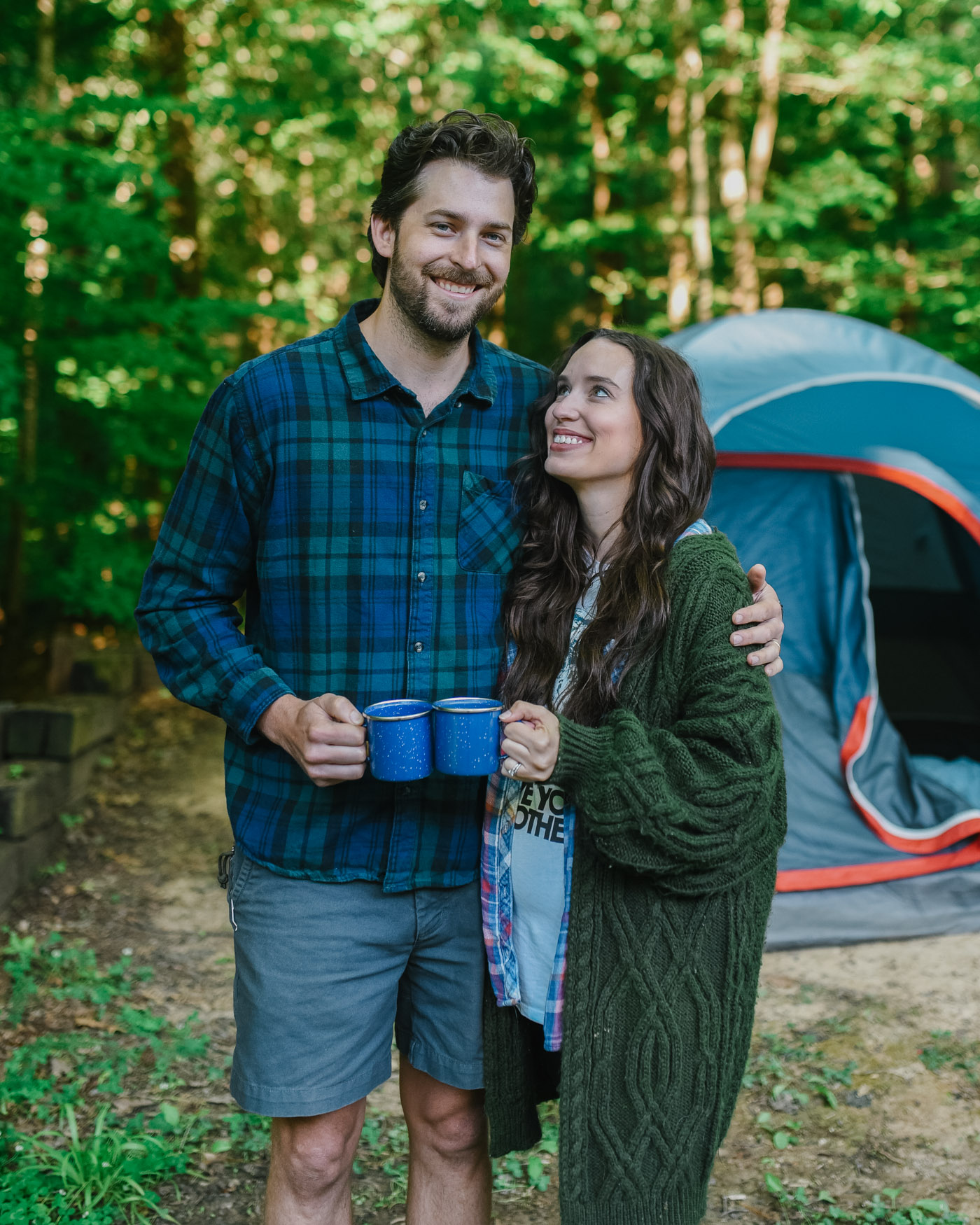 Father's Day Gift Ideas by popular Memphis lifestyle blog, Lone Star Looking Glass: image of a husband and wife standing together in front of their Coleman tent while holding blue enamel wear mugs. 