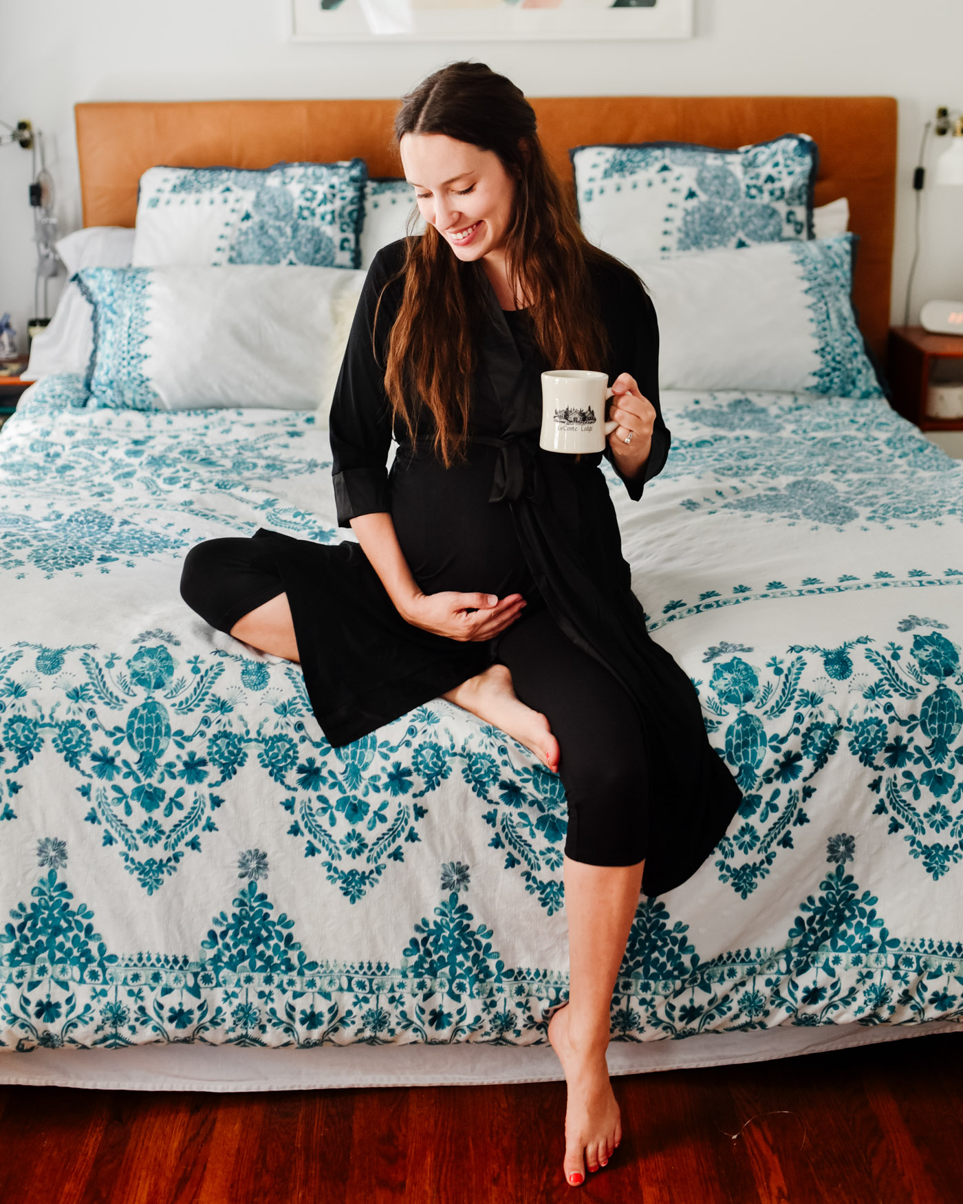 Maternity Pajamas by popular Memphis fashion blog, Lone Star Looking Glass: image of a woman sitting on her bed while holding a coffee mug and wearing a Kindread Bravely Emmaline Robe. 