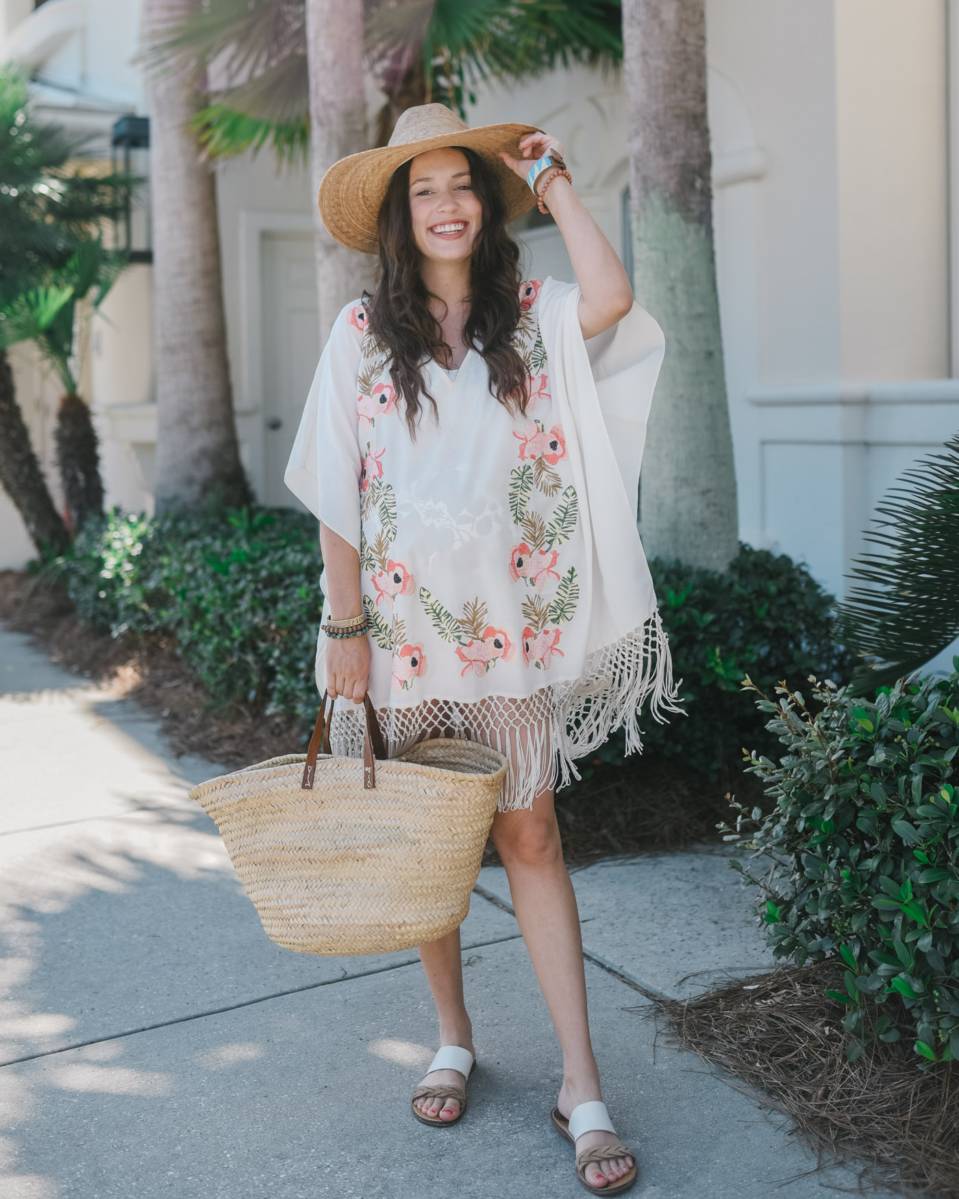 maternity beach swim cover up show me your mumu pink embroidered fringe caftan | Maternity Style by popular Memphis fashion blog, Lone Star Looking Glass: image of a woman walking outside on a palm tree lined sidewalk while wearing a Show Me Your Mumu Maleia Tunic, Madwell WYETH™ Straw Ipanema Hat, ShopBop Soludos Braided Slide Sandals, and holding a Amazon Moroccan Straw Market Bag w/Blue Leather Strip Handles. 