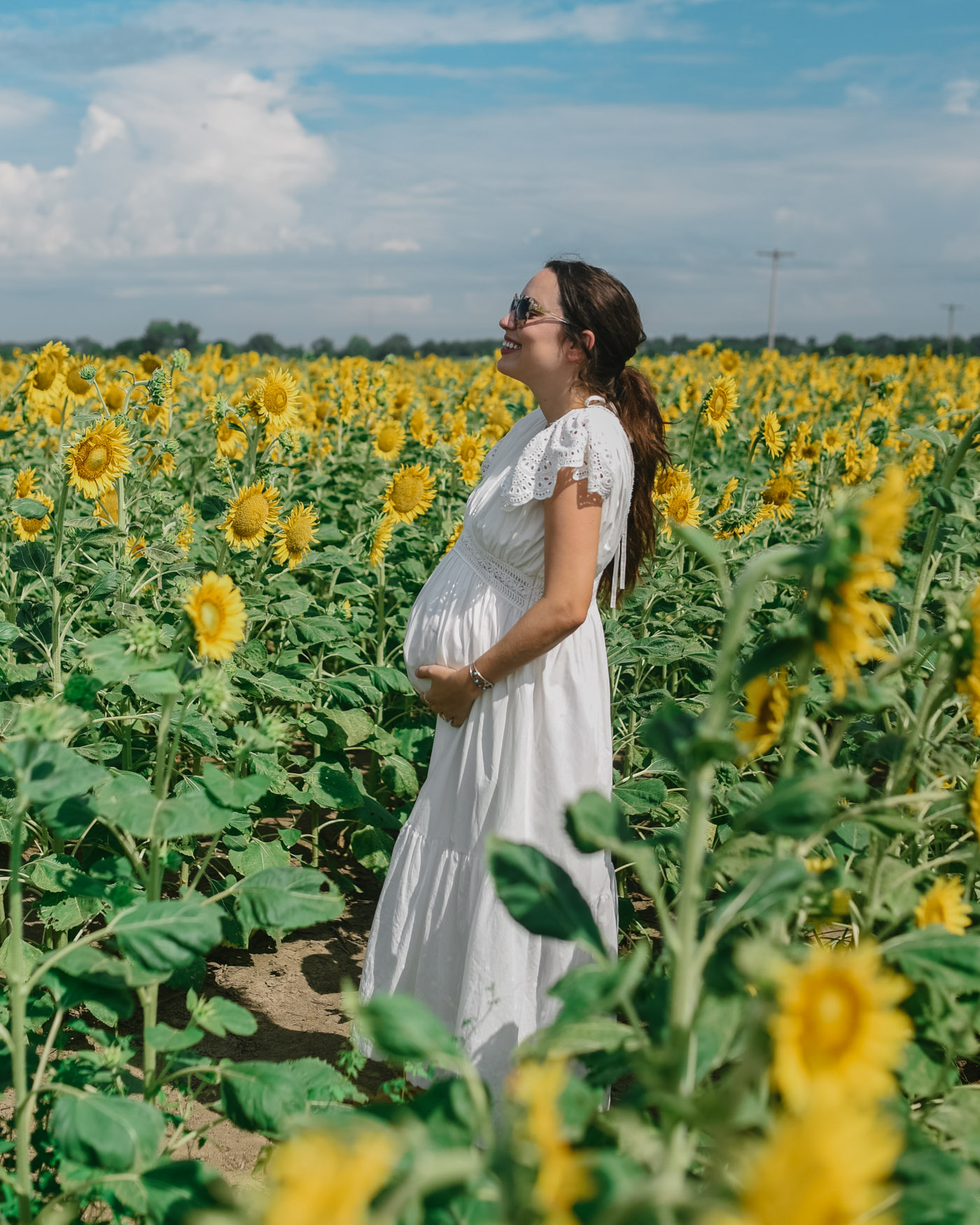 30 Weeks Pregnant by popular Memphis motherhood blog, Lone Star Looking Glass: image of a woman standing in a field of sunflowers and wearing a ChicWish FRILL HEM PLUNGING V-NECK SLEEVELESS MAXI DRESS IN WHITE, Swedish Hasbeens Kringlan, and Free People Western Cuff Set.