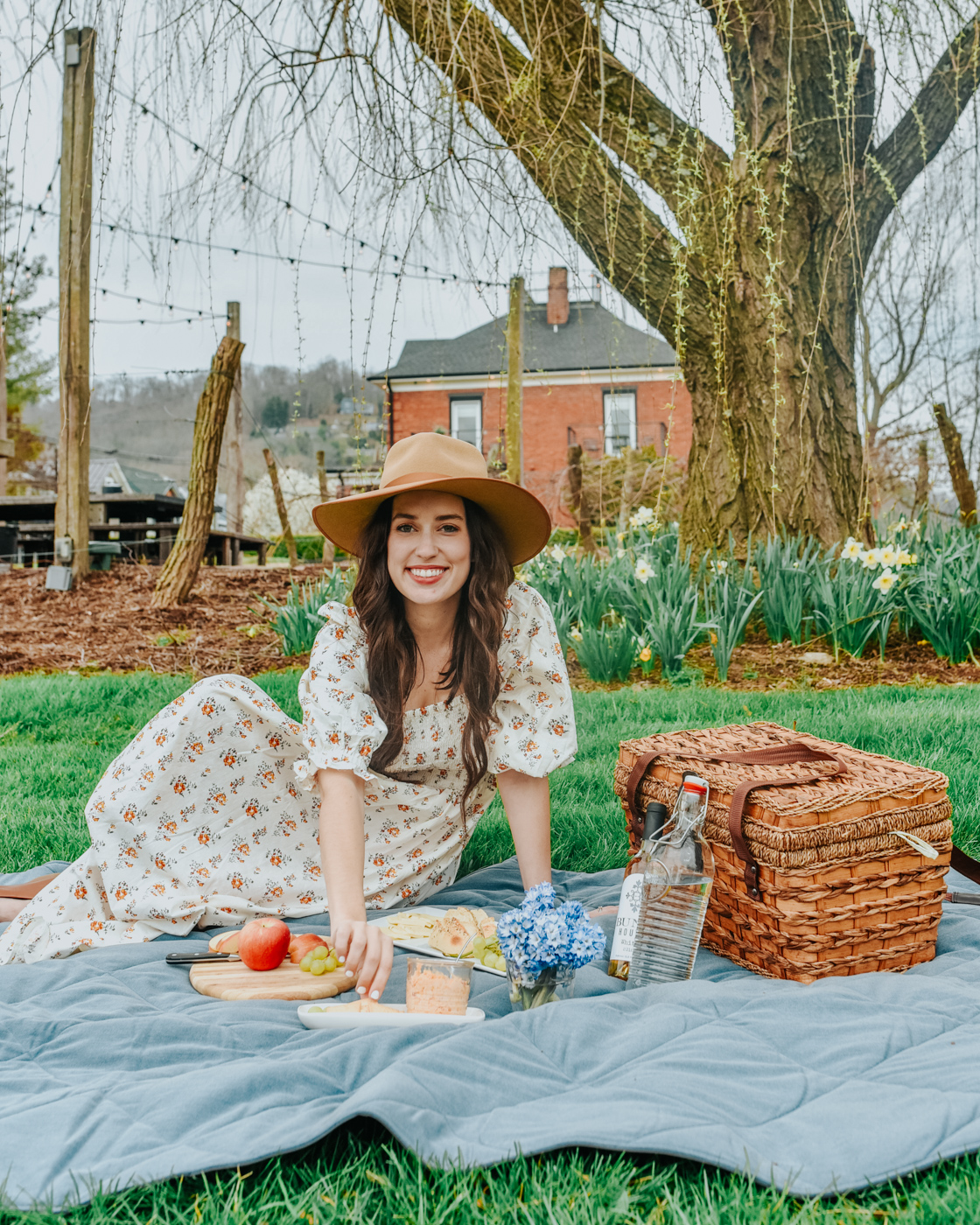 Bunn House by popular Memphis travel blog, Lone Star Looking Glass: image of a woman sitting outside on a picnic blanket near the Bunn House and wearing a Lack of Color hat and floral puff sleeve maxi dress. 