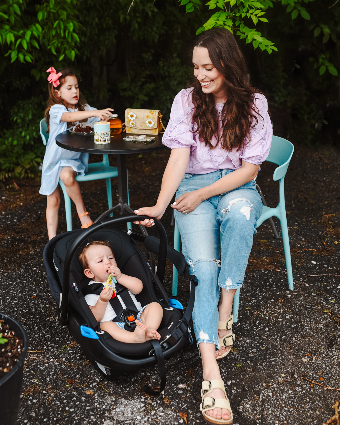 Maxi Cosi Coral XP Car Seat by popular Memphis motherhood blog, Lone Star Looking Glass: image of a mom sitting outside at a bistro style table with her daughter and rocking her son in a Maxi Cosi Coral XP carseat. 