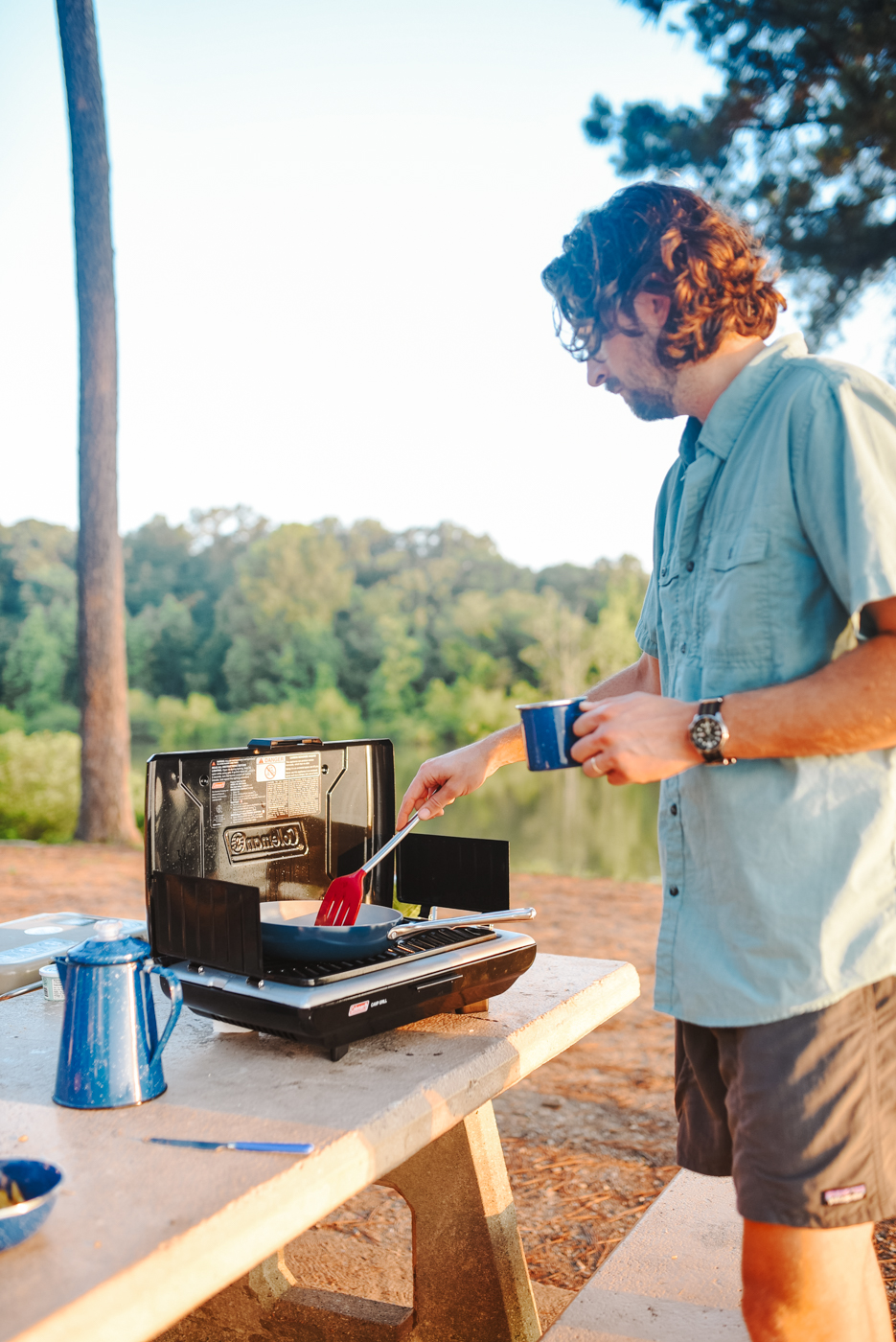 Camping With Kids by popular Memphis lifestyle blog, Lone Star Looking Glass: image of a man cooking food on a portable Coleman camping stove. 