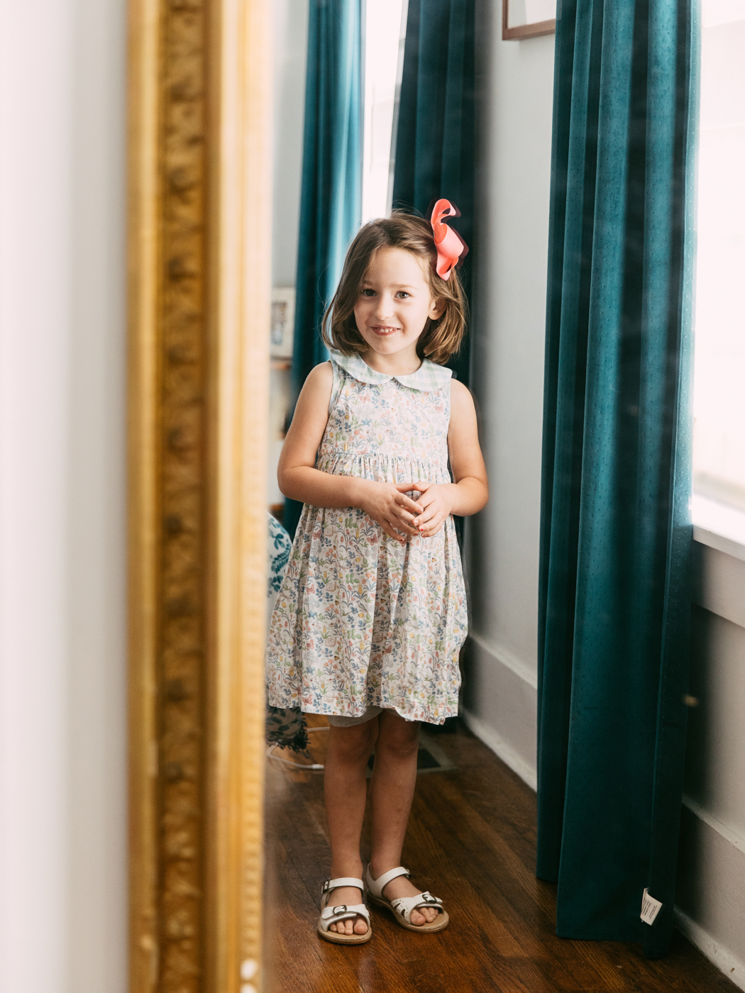 Antique Pier Mirror by popular Memphis life and style blog, Lone Star Looking Glass: image of a little girls wearing a pair white sandals, pink hair bow and floral pink dress and looking at herself in a antique pier mirror. 