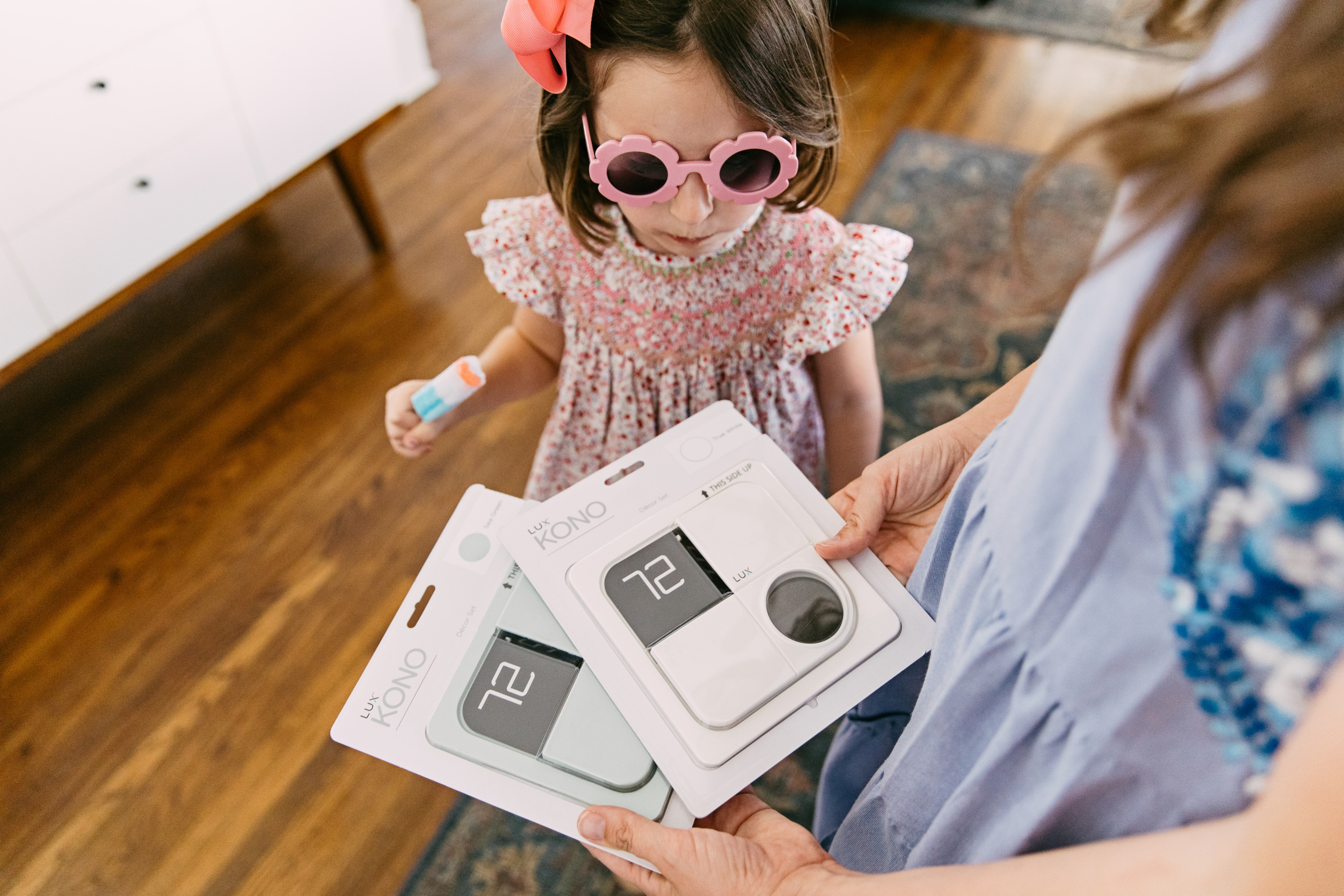 Lux Kono Smart Thermostat by popular Memphis lifestyle blog: image of a little girl wearing pink flower frame sunglasses and holding a rocket popsicle while looking at Lux Kono smart thermostat products with her mom. 