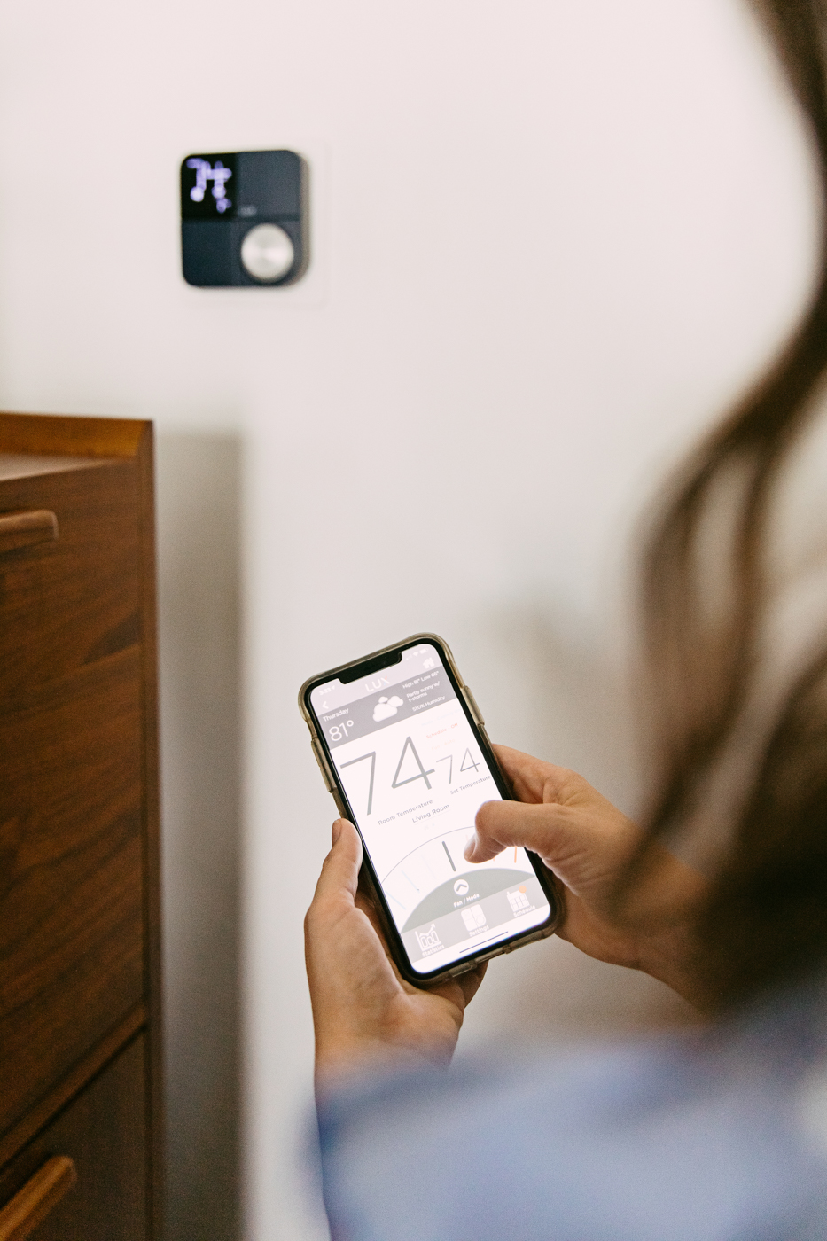 Lux Kono Smart Thermostat by popular Memphis lifestyle blog: image of a woman looking at a Lux Kono smart thermostat on her smartphone. 