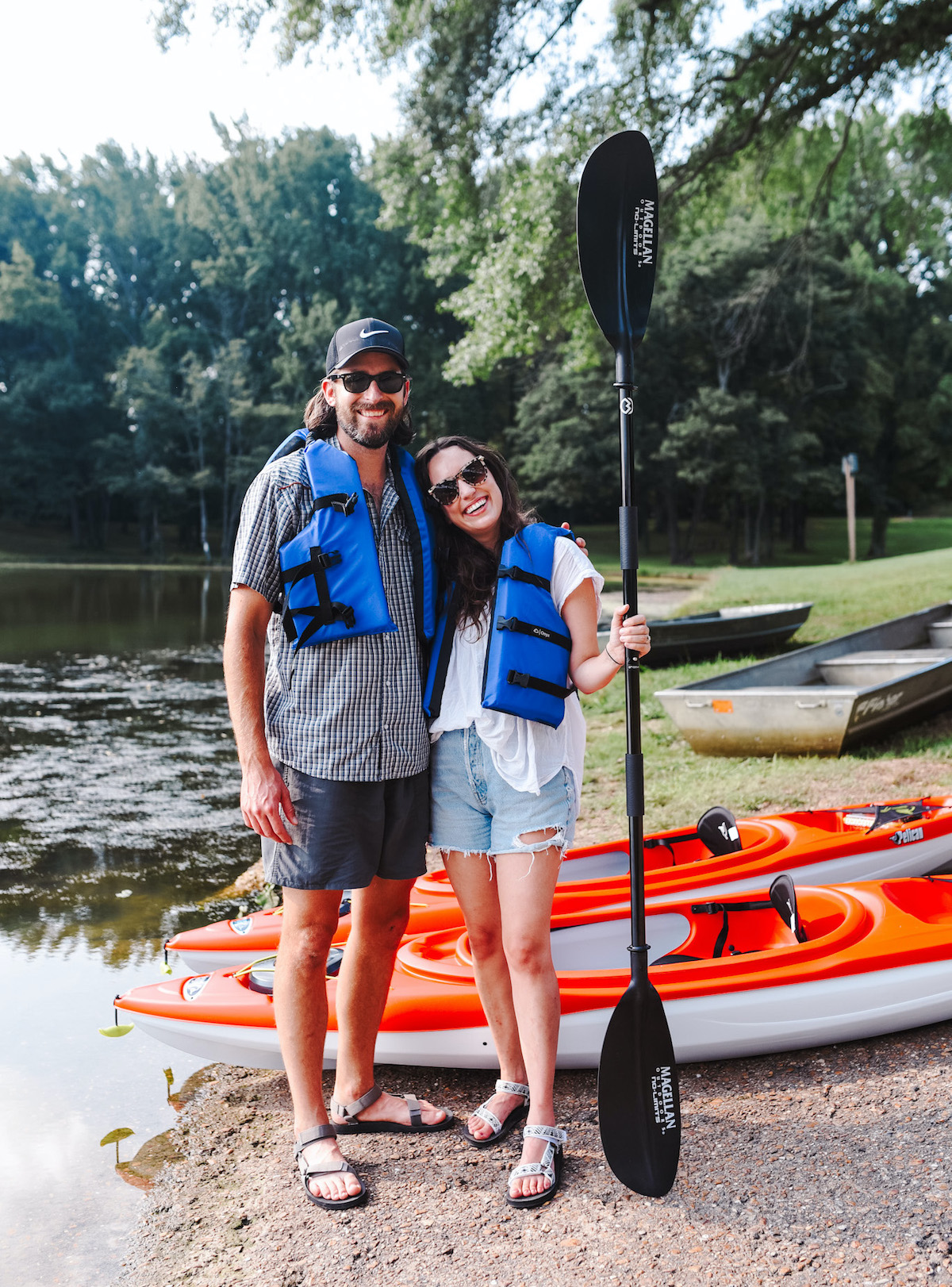Kayaking for Beginners by poplar Memphis lifestyle blog, Lone Star Looking Glass: image of a husband and wife standing together and wearing blue lifejackets while standing next to some red kayaks. 