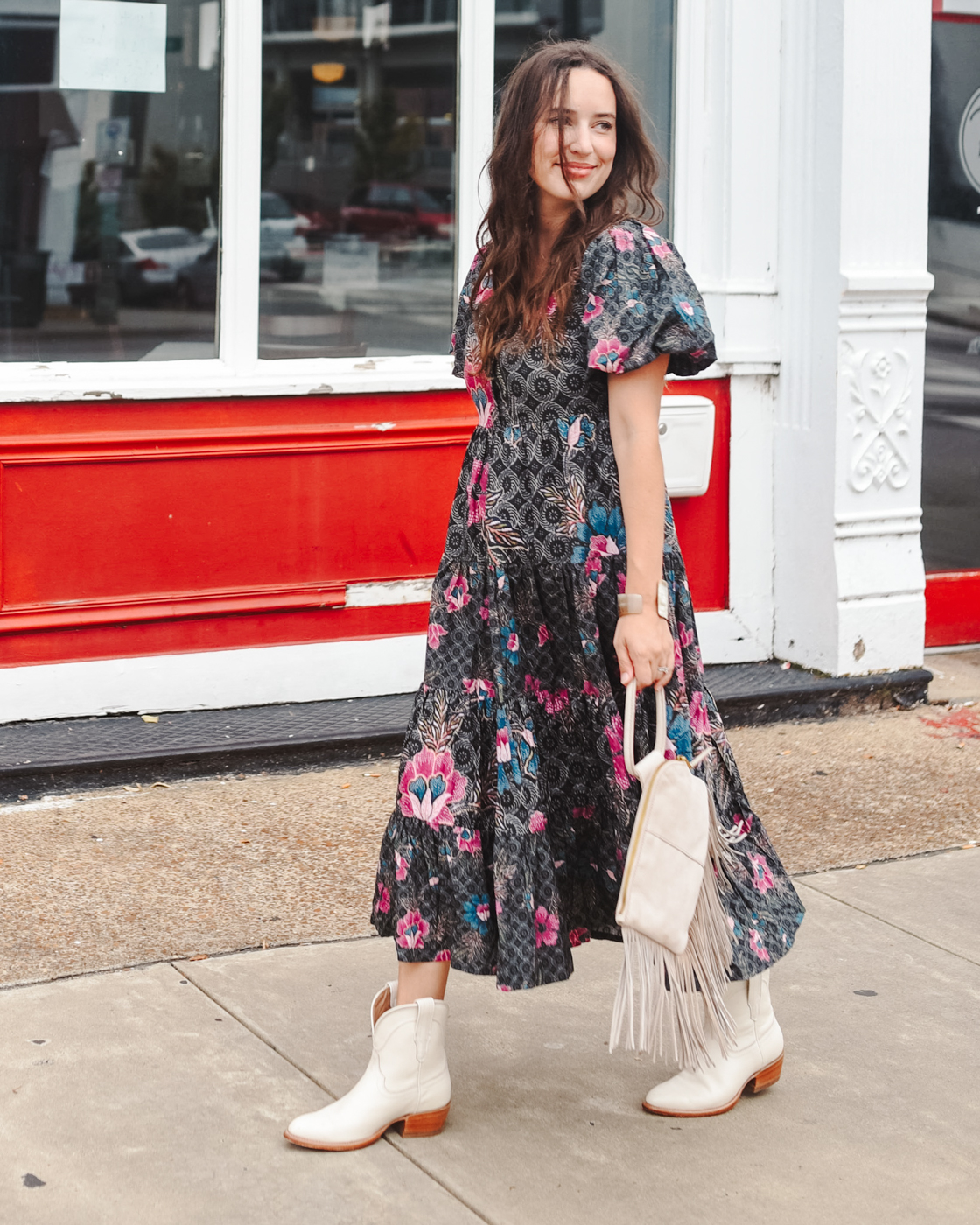 Western Boots by popular Memphis fashion blog, Lone Star Looking Glass: image of a woman walking outside and wearing a black and pink floral print tiered midi dress with a pair of white western boots. 
