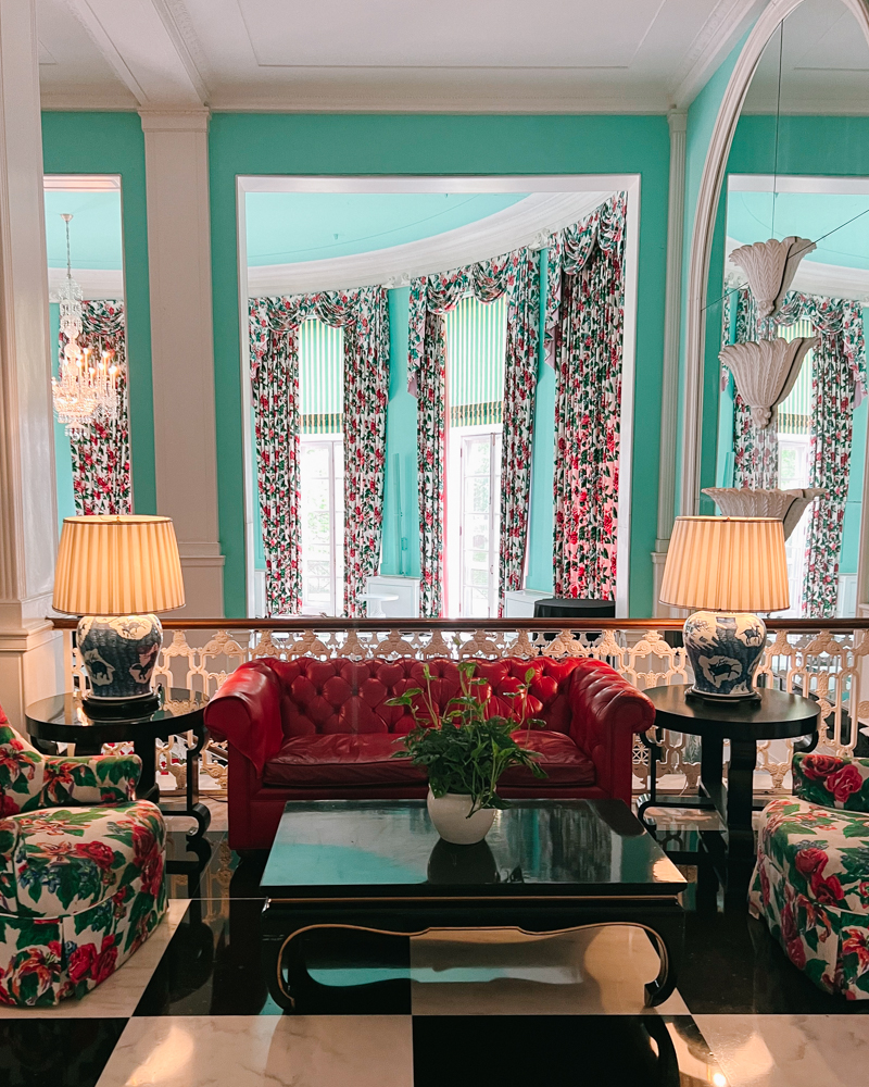 Classic Dorothy Draper interiors at The Greenbrier featuring floral armchairs and a red Chesterfield sofa.