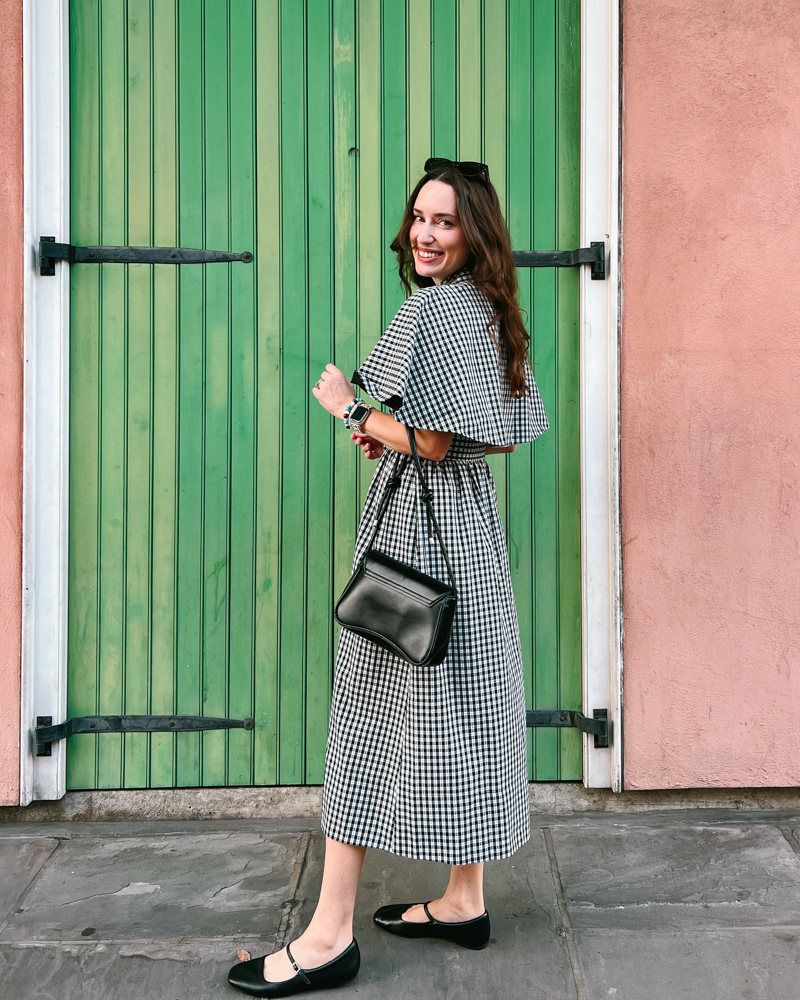 Woman wearing black gingham cape sleeve Tuckernuck dress with black Mary Jane flats and vintage handbag in the French Quarter