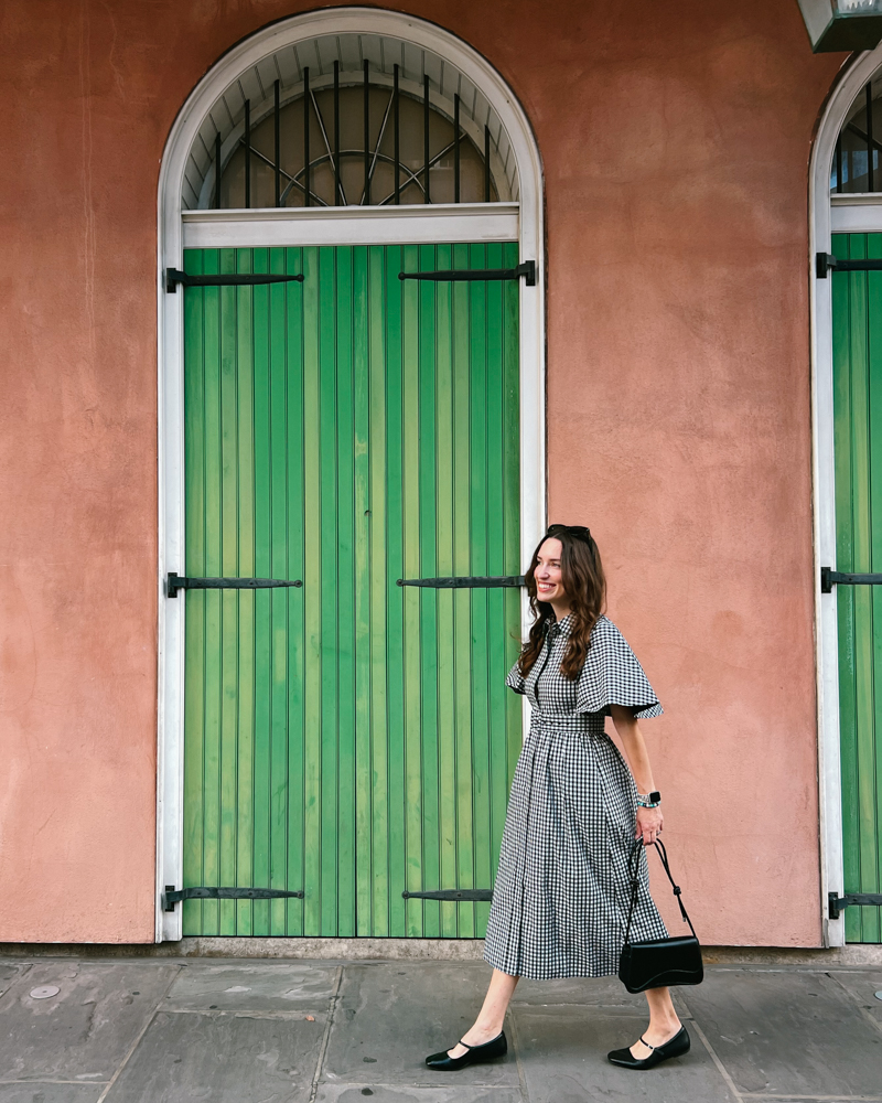 Woman wearing black gingham cape sleeve Tuckernuck dress with black Mary Jane flats and vintage handbag in the French Quarter