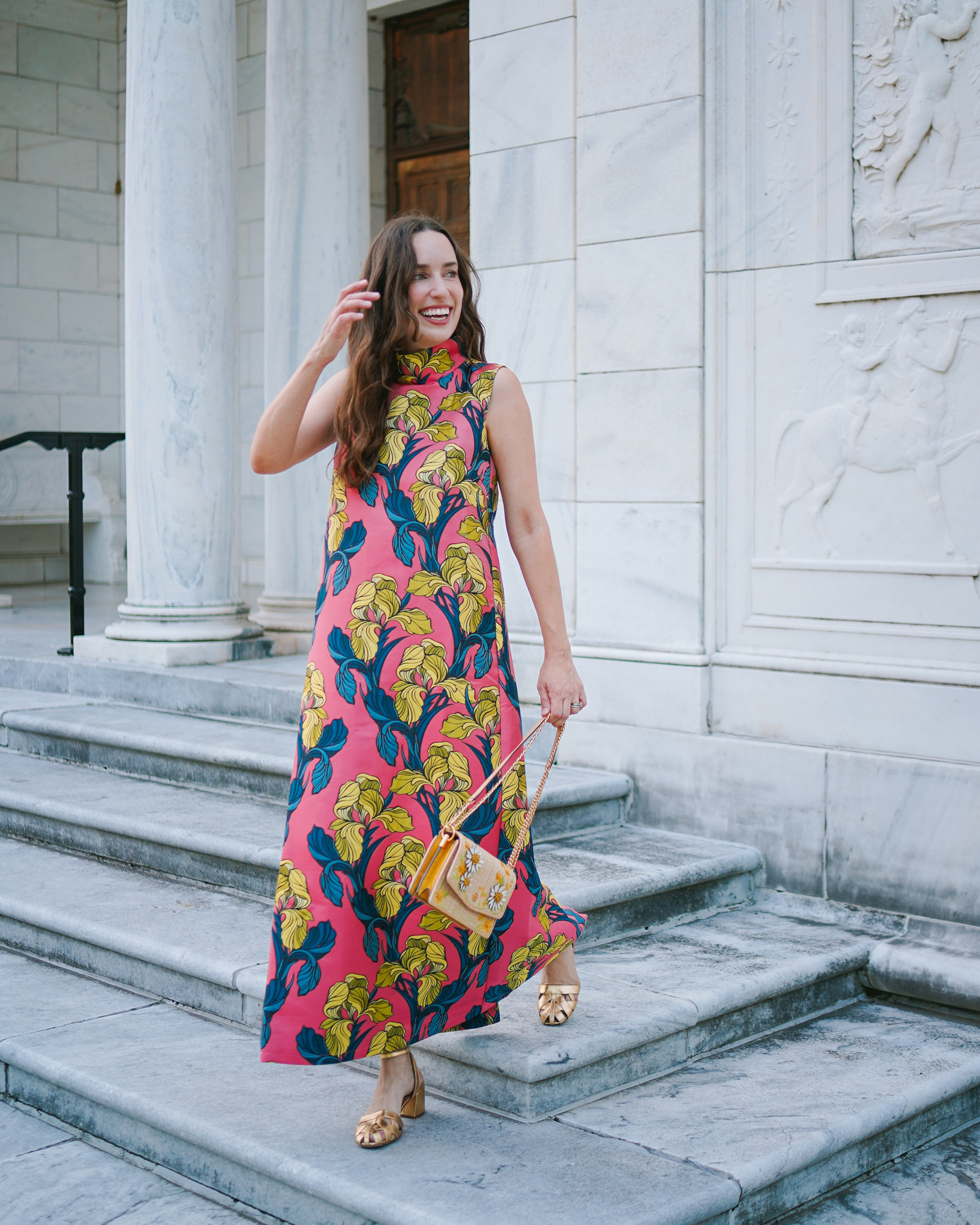 colorful coral floral jacquard BURU maxi dress with gold heels on marble steps.