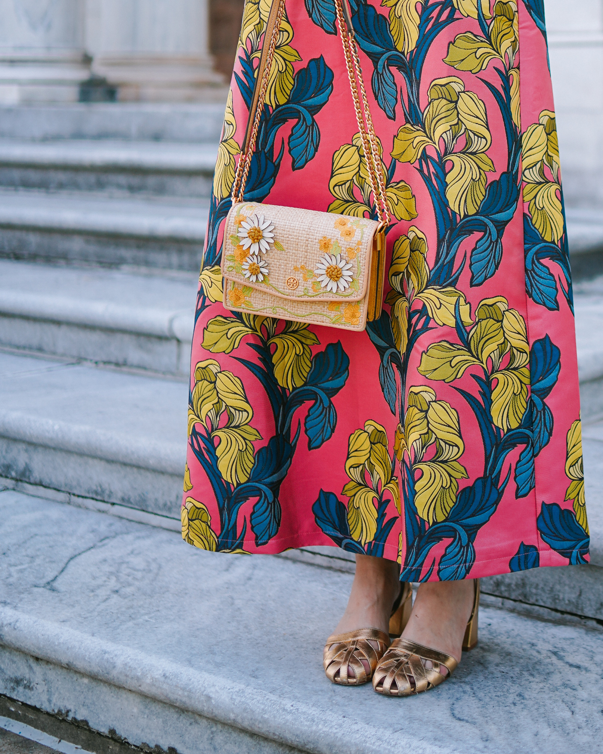 Close-up of a floral evening bag and metallic gold heels styled with a coral iris print maxi dress.